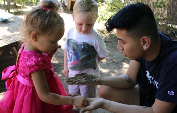 Two children exploring dirt and sand with their caregiver.